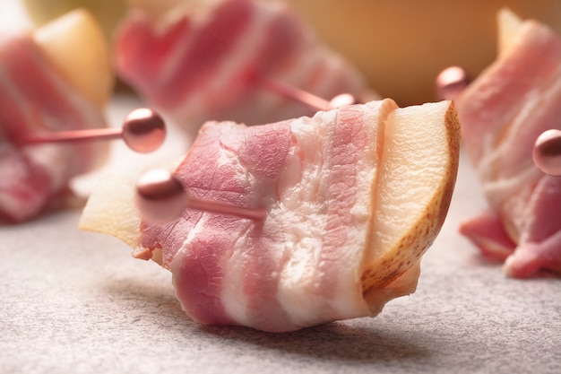 De fines tranches de bacon rose sur des brochettes dans une poire avec du fromage à pâte molle