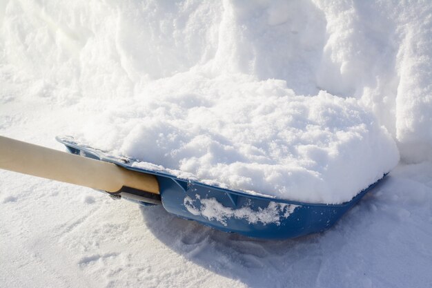 Finir de pelleter la neige dans le trottoir. Pelle à neige près d'un grand banc de neige pendant le nettoyage