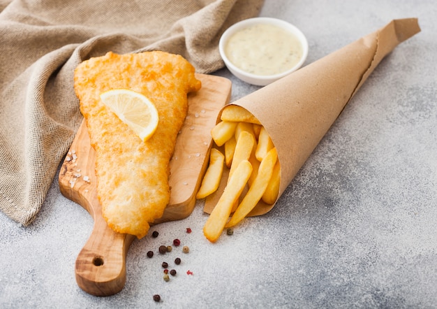 Fish and Chips britannique traditionnel avec sauce tartare sur planche à découper sur tableau blanc.