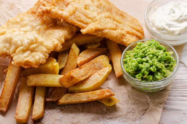 Fish and chips de cuisine de rue britannique traditionnelle avec purée de petits pois et sauce tartare sur papier parchemin