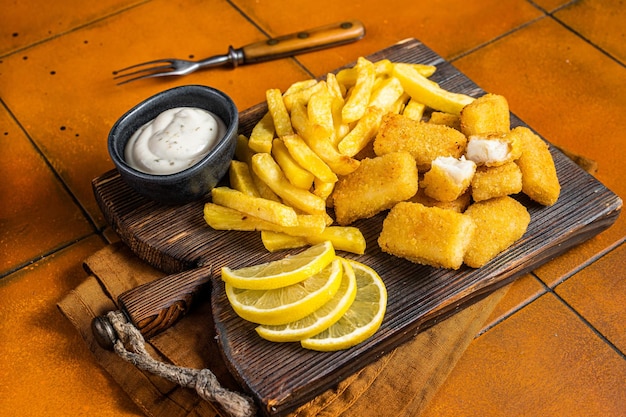 Fish and Chips Fastfood britannique Bâtonnets de poisson avec frites sur planche de bois Fond orange Vue de dessus