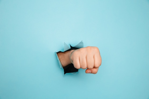 Fist poinçonnage à travers le mur de papier bleu. Menace, combat et sports de combat. Poussez à travers le mur