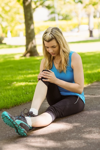 Fit blonde touchant son genou blessé sur le chemin