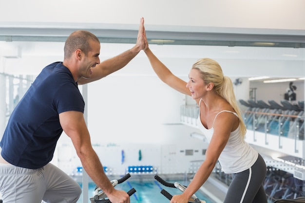 Fit couple donnant cinq haut tout en travaillant sur des vélos d&#39;exercice au gymnase