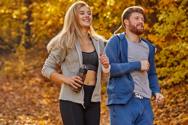 Fit couple entraînement jogging est journée d'automne ensoleillée à l'extérieur, athlétique caucasien homme et femme. couple actif jogging