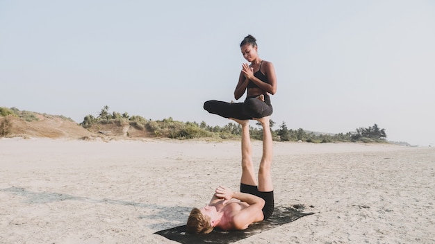 Fit couple sportif pratiquant l'acro yoga avec partenaire ensemble sur la plage de sable.