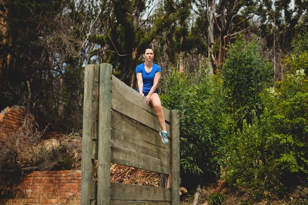 Fit femme assise sur un obstacle de mur en bois