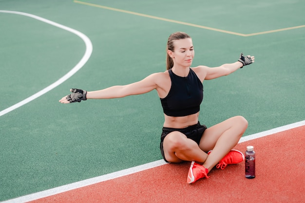 Fit femme sportive l'eau potable de la bouteille sur le stade pendant l'entraînement de fitness