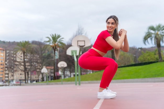 Fit femme en tenue rouge faisant des squats dans un parc de la ville fitness et concept actif sain