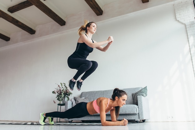 Fit les femmes à la maison d'entraînement. Fille sautant par-dessus son amie tandis que la femme effectuant la position de la planche.