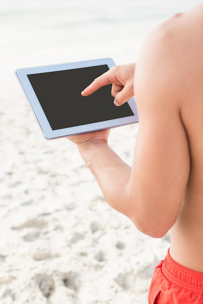 Fit homme à l'aide de tablette sur la plage