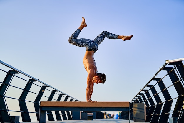 Fit l'homme faisant un stand de main tout en pratiquant le yoga seul près de l'océan contre le ciel au crépuscule ou à l'aube