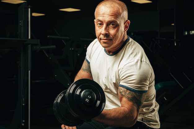 Fit l'homme senior exerçant avec des haltères dans une salle de sport