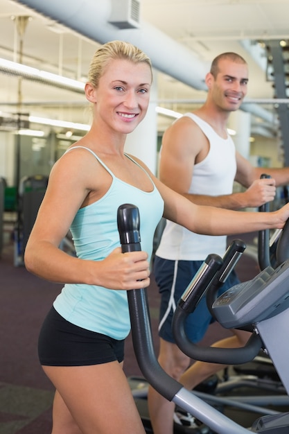 Fit jeune couple travaillant sur x-trainers au gymnase