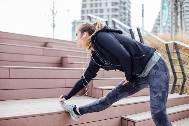 Fit la jeune femme avec des écouteurs faisant des exercices d'étirement dans les escaliers à l'extérieur