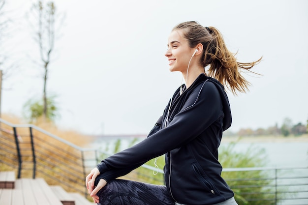 Fit la jeune femme avec des écouteurs faisant des exercices d'étirement dans les escaliers à l'extérieur