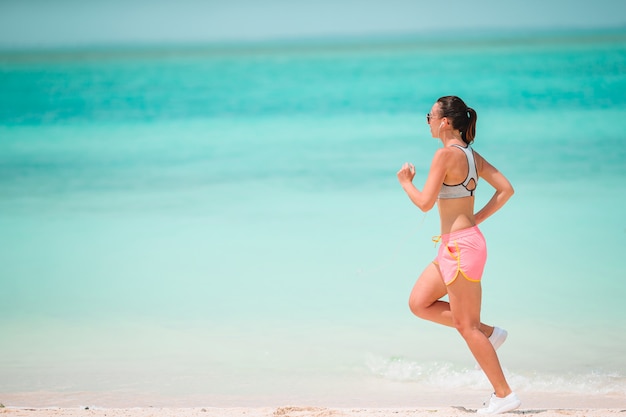 Fit la jeune femme faisant des exercices sur la plage blanche tropicale dans ses vêtements de sport