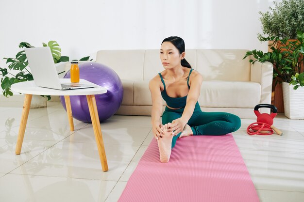 Fit une jeune femme mince tendant une jambe et se penchant vers l'avant en regardant une vidéo sur un ordinateur portable