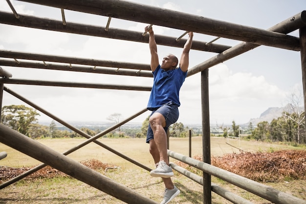 Fit man escalade des barres de singe pendant la course d'obstacles dans le camp d'entraînement