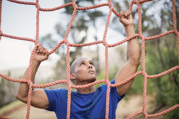 Fit man escalade un filet pendant la course d'obstacles dans le camp d'entraînement