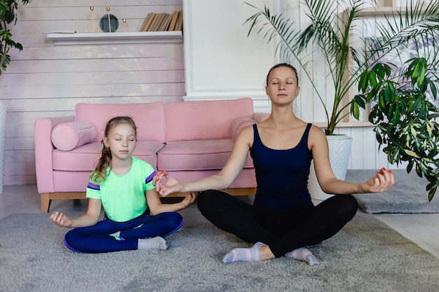 Fit mère et fille faisant du yoga ou de la méditation dans le salon. Sports à domicile. Famille faisant du sport ensemble à la maison. Concept de yoga et de famille.