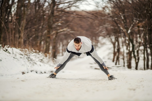 Fit sportif faisant des exercices d'étirement et d'échauffement tout en se tenant dans la nature lors d'une journée d'hiver enneigée. Fitness en plein air, fitness d'hiver, mode de vie sain