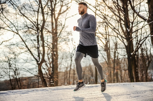 Fit sportif jogging dans la nature au jour d'hiver enneigé. Temps froid, fitness hivernal, exercices cardio