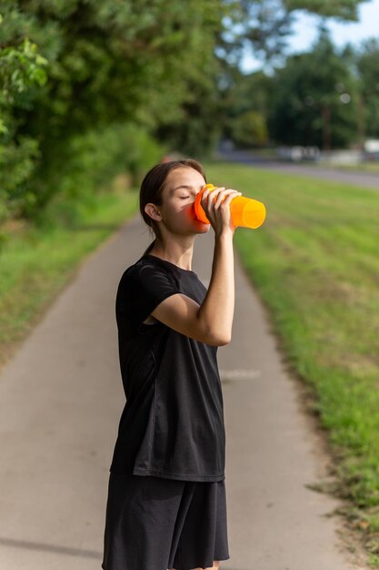 Fit tennage girl runner à l'extérieur tenant une bouteille d'eau Fitness femme prenant une pause après avoir couru l'entraînement