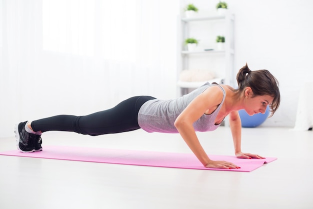 Fit woman doing pushups sur le sol dans son salon un tapis d'exercice à la maison