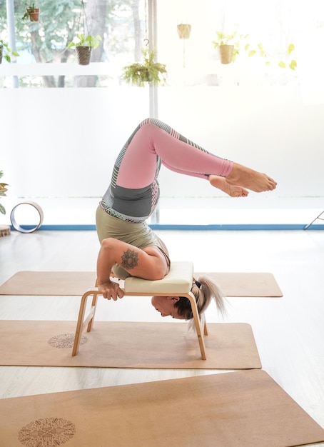 Fit woman in headstand à l'aide d'un banc de yoga professionnel pieds nus dans la posture de criquets inversés Viparita Salabhasana