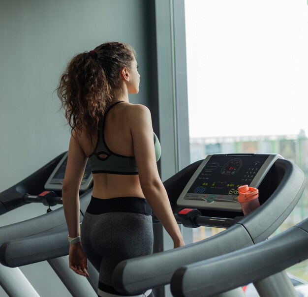 Fit woman in sportswear s'exécute sur un tapis roulant et regarde sa montre dans la salle de gym. Le concept d'un mode de vie sain, échauffement, remise en forme, perte de poids.