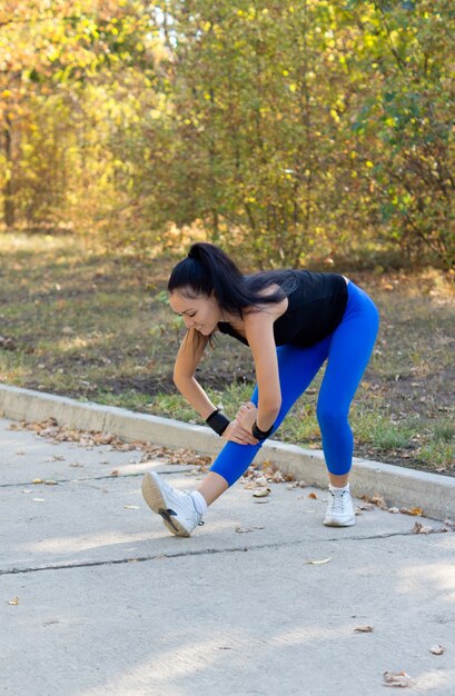 Fit young woman assouplir étirant ses muscles avant de commencer son entraînement sur une route goudronnée à travers un parc