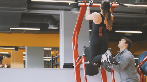 Fitness-club - jeune femme exécute des tractions avec entraîneur masculin - vue arrière, vue rapprochée