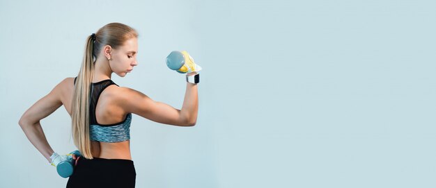 Fitness femme blonde debout avec des haltères dans le dos