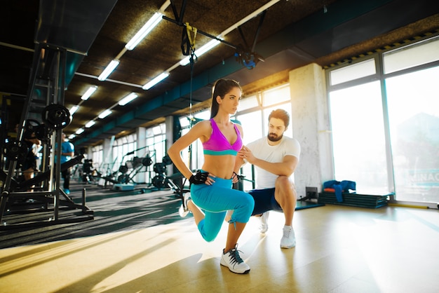 Fitness fille mince faisant une jambe qui s'étend avec une corde du haut et l'aide d'un entraîneur personnel dans la salle de gym.