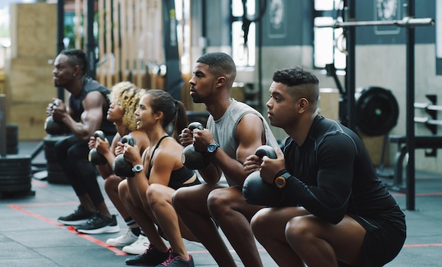 Photo fitness d'haltérophilie et personnes avec une cloche de bouilloire dans la salle de gym pour l'exercice d'entraînement et la classe d'entraînement travail d'équipe constructeur de corps et hommes et femmes s'accroupissent avec des poids pour défier le bien-être et la force
