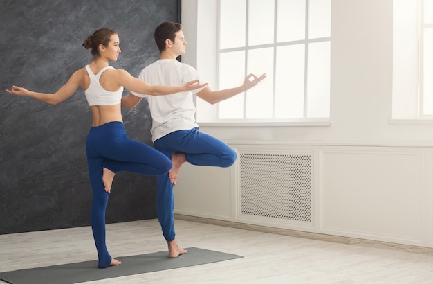 Fitness, homme et femme faisant du yoga dans une pose d'arbre. Un jeune couple fait un exercice de détente à la fenêtre, vue arrière, espace de copie