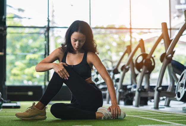 Fitness jeune femme qui s'étend de sa jambe pour se réchauffer au sol au club de sport gym