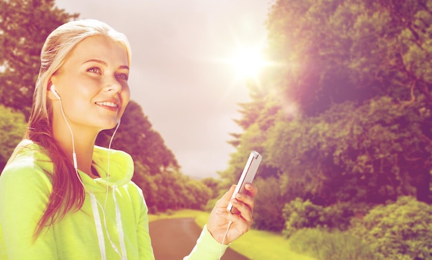 fitness, sport, entraînement, technologie et concept d'exercice - femme sportive avec smartphone et écouteurs écoutant de la musique à l'extérieur sur la route et sur fond naturel