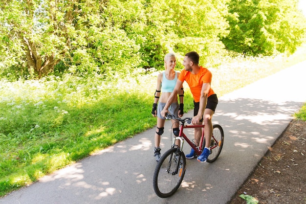 fitness, sport, été, personnes et concept de mode de vie sain - couple heureux avec rollers et vélo et parler à l'extérieur en été