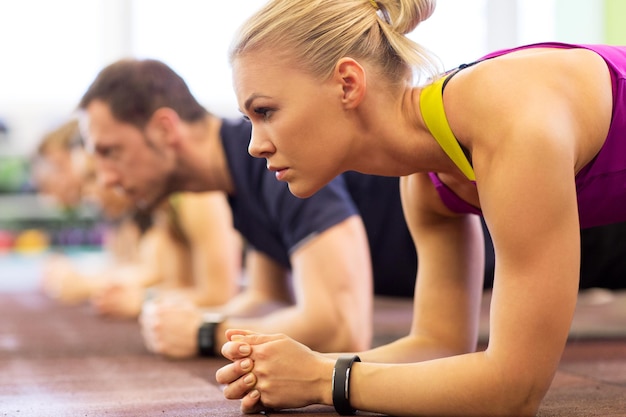 fitness, sport, exercice, personnes et style de vie sain concept - gros plan d'une femme avec un traqueur de fréquence cardiaque à l'entraînement de groupe faisant un exercice de planche dans le gymnase