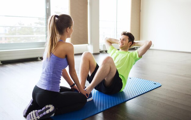 fitness, sport, formation, travail d'équipe et concept de personnes - femme avec entraîneur personnel faisant des redressements assis dans la salle de gym