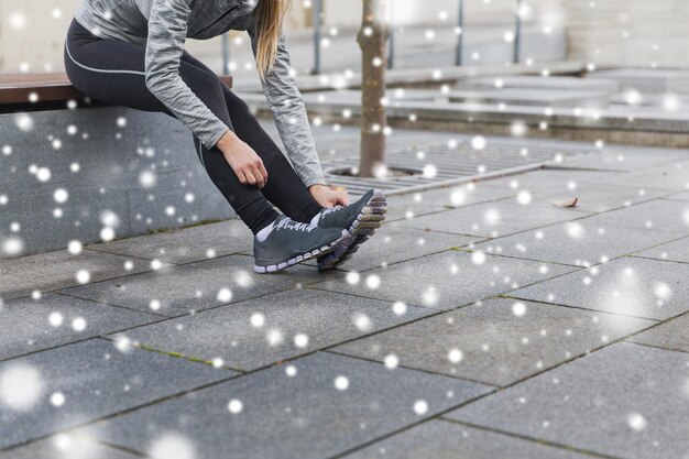 Photo fitness, sport, personnes et style de vie sain concept - gros plan d'une jeune femme sportive attachant ses chaussures à l'extérieur sur la neige
