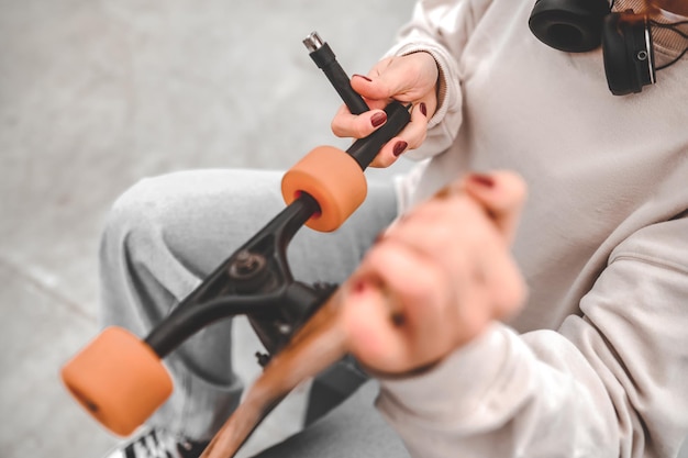 Fixation. Mains de fille en sweat-shirt gris et jeans fixant la roue sur une planche à roulettes, se tordant avec un outil spécial, pas de visage