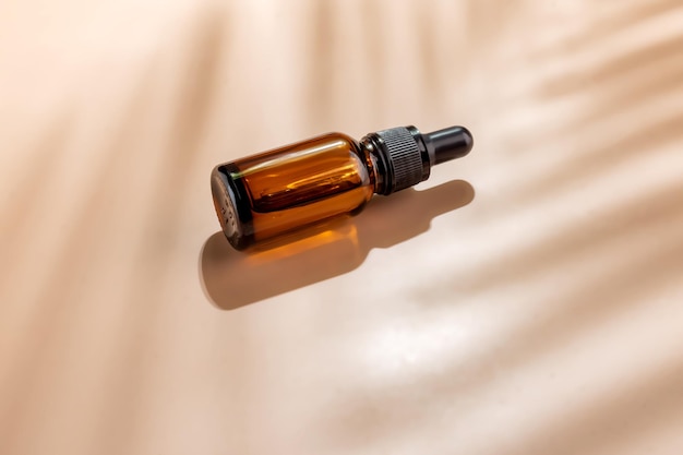 Flacon compte-gouttes cosmétique en verre ambré avec étiquette vierge sur fond beige avec ombre de feuille de palmier Marque de conception de produits de beauté à la mode Cosmétiques maquette