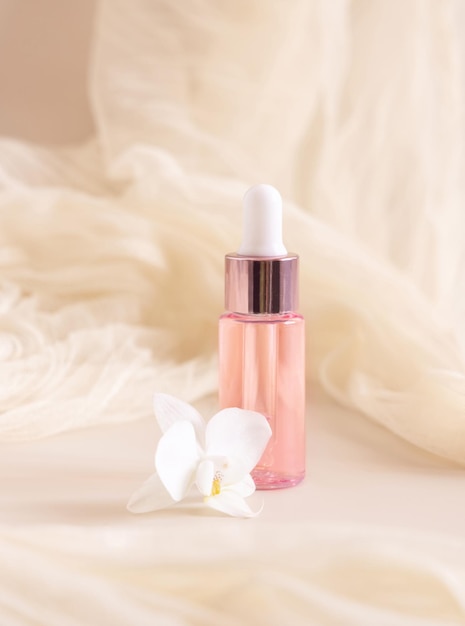 Flacon compte-gouttes rose près d'une fleur d'orchidée blanche sur un gros plan jaune clair Produit de beauté pour le soin de la peau
