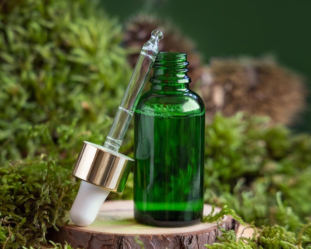 Flacon compte-gouttes vert ouvert sur un morceau de bois entre une maquette cosmétique naturelle en gros plan de mousse verte