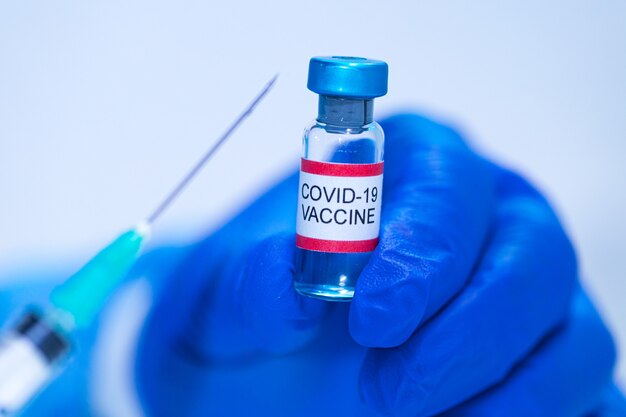 Flacon contenant le vaccin contre le COVID-19 tenu par la main d'un médecin et dans l'autre main une seringue. Concept de vaccination contre le coronavirus