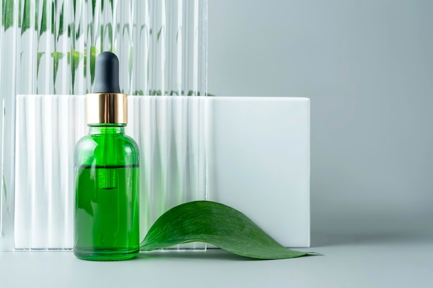 Photo flacon cosmétique en verre vert avec pipette à côté du podium blanc et emballage de produit de fenêtre en verre avec sérum anti-âge de branche de ruscus naturel avec concept de spa de maquette de peptides cosmétiques