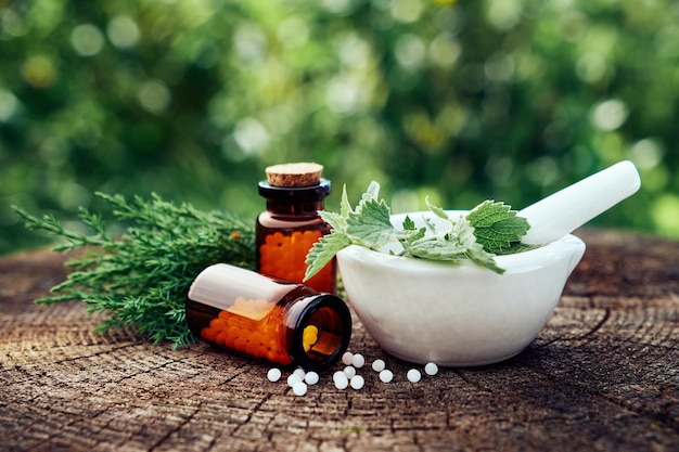 Photo flacon de globules homéopathiques mortier d'ortie verte et feuilles de menthe brindilles de genévrier homéopathie